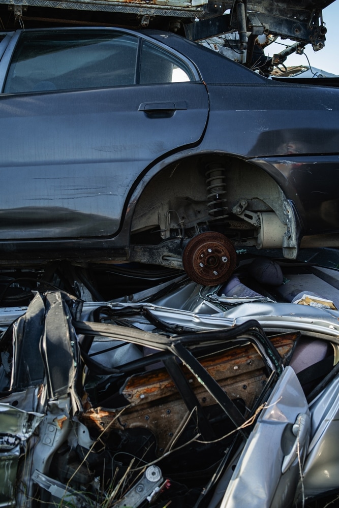 Casse automobile : voitures accidentées et ferraille Voitures empilées dans une casse automobile avec berline grise, disque de frein rouillé et débris de métal.
