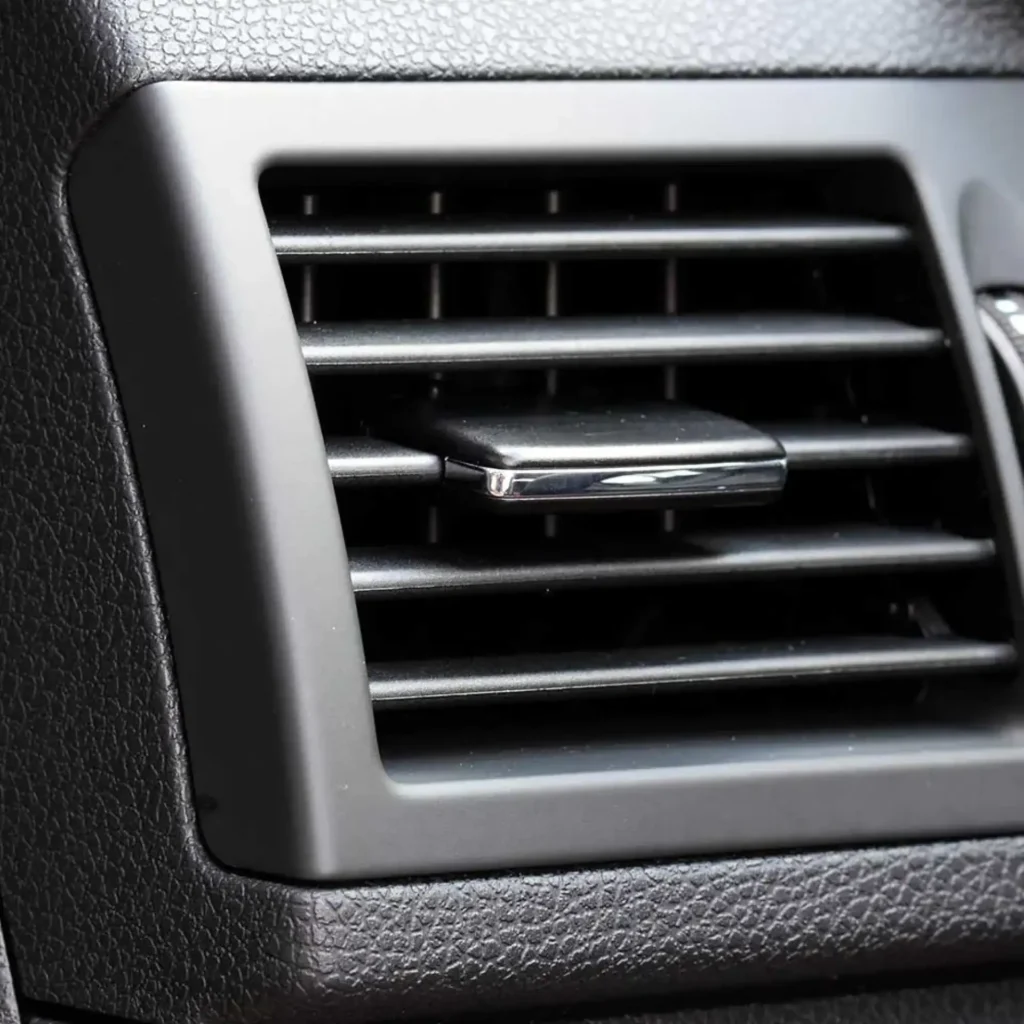 Grille d'aération de voiture noire avec curseur de réglage chromé sur un tableau de bord texturé.