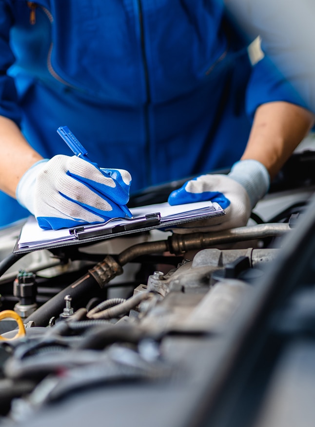 Entretien voiture : révision complète du moteur au garage Mécanicien en bleu de travail remplissant un carnet d'entretien lors d'une révision du moteur d'une voiture au garage.