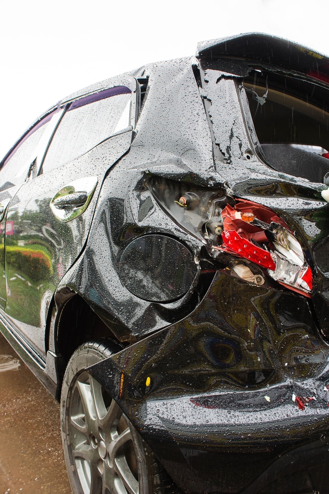 Voiture noire accidentée : dégâts importants sur l'arrière Voiture noire accidentée : aile arrière enfoncée, feu arrière brisé et dégâts importants sur la carrosserie.