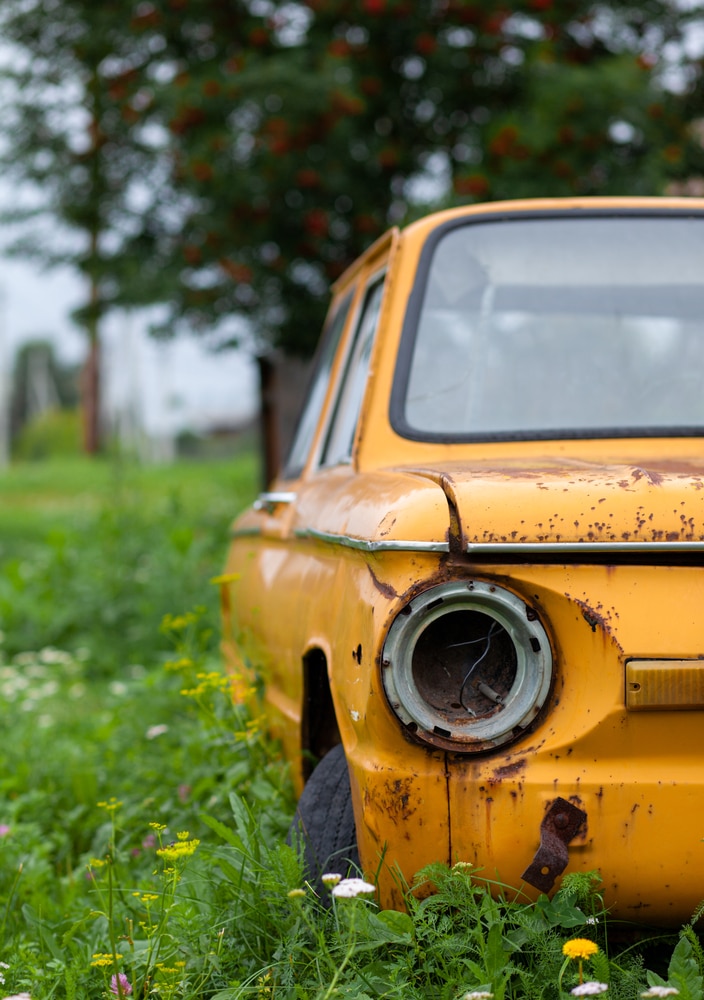 Voiture Jaune Vintage Abandonnée dans un Champ Fleuri Voiture vintage jaune abandonnée et rouillée dans un champ de fleurs sauvages avec phare manquant.